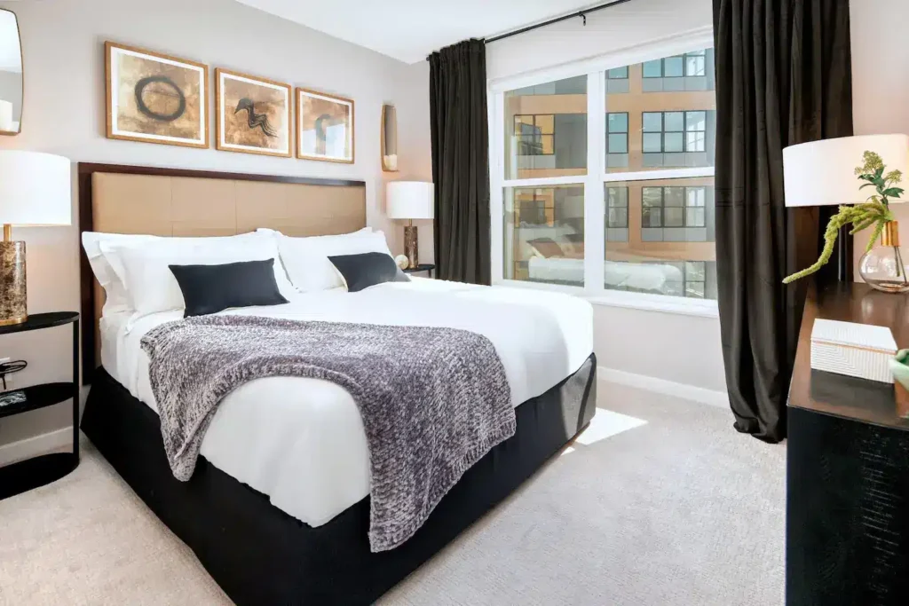 Modern furnished bedroom with large window, cozy bedding, and stylish décor – Hyatus Living apartment.